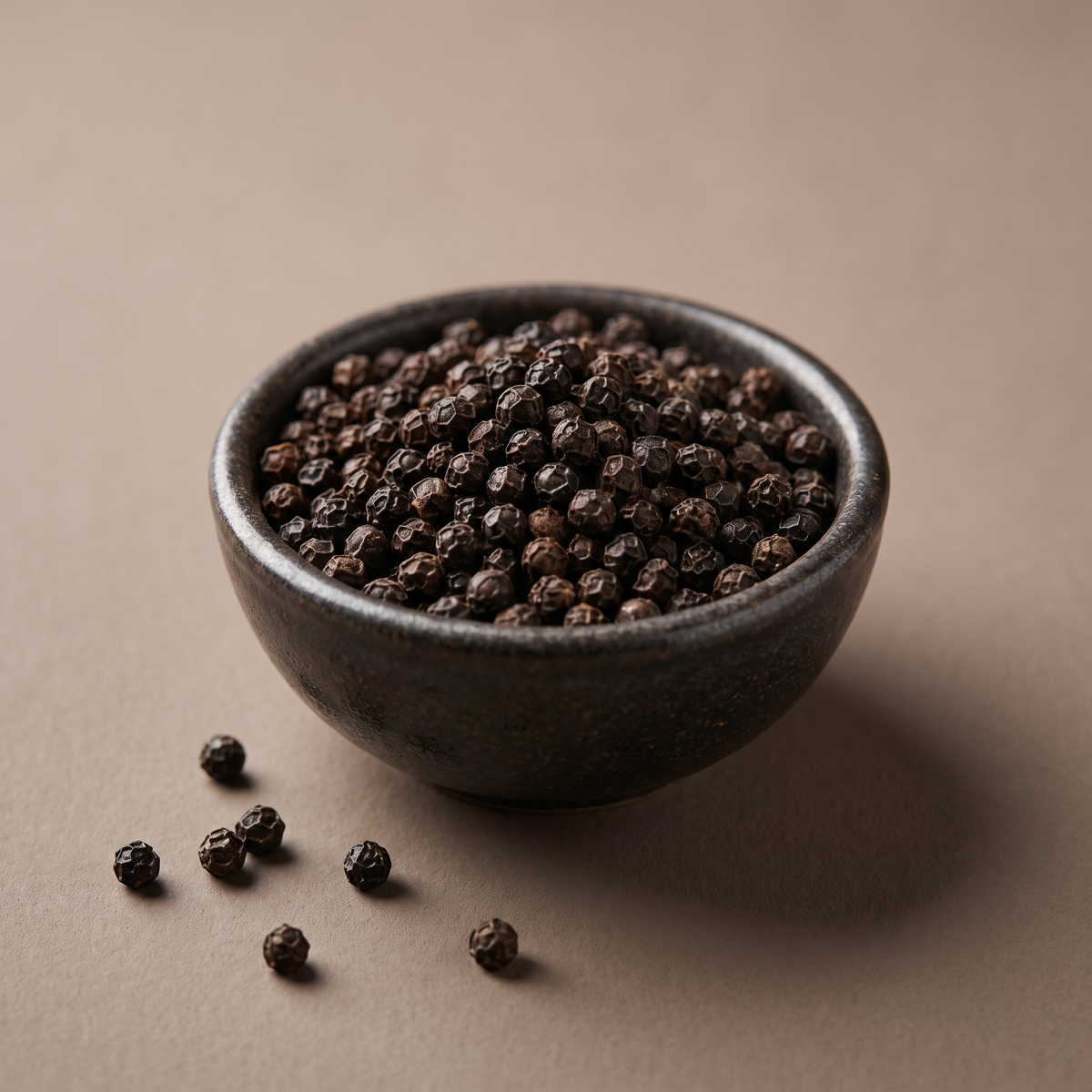 Whole black peppercorns in a dark ceramic bowl