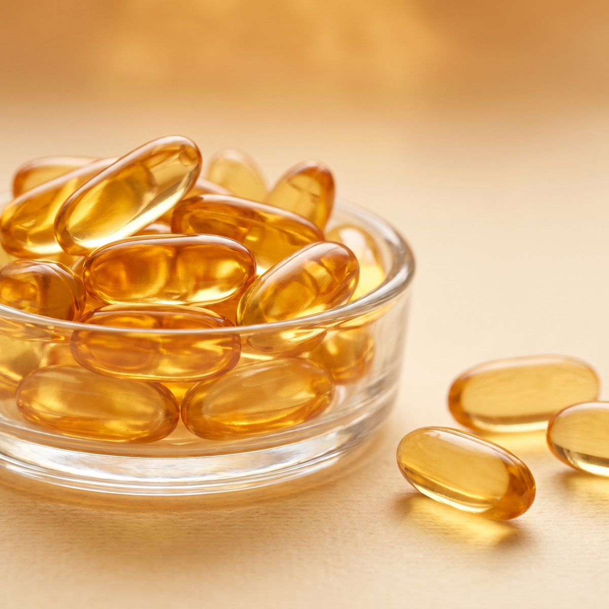 Coenzyme Q10 amber softgel capsules in a glass bowl on a warm gold background